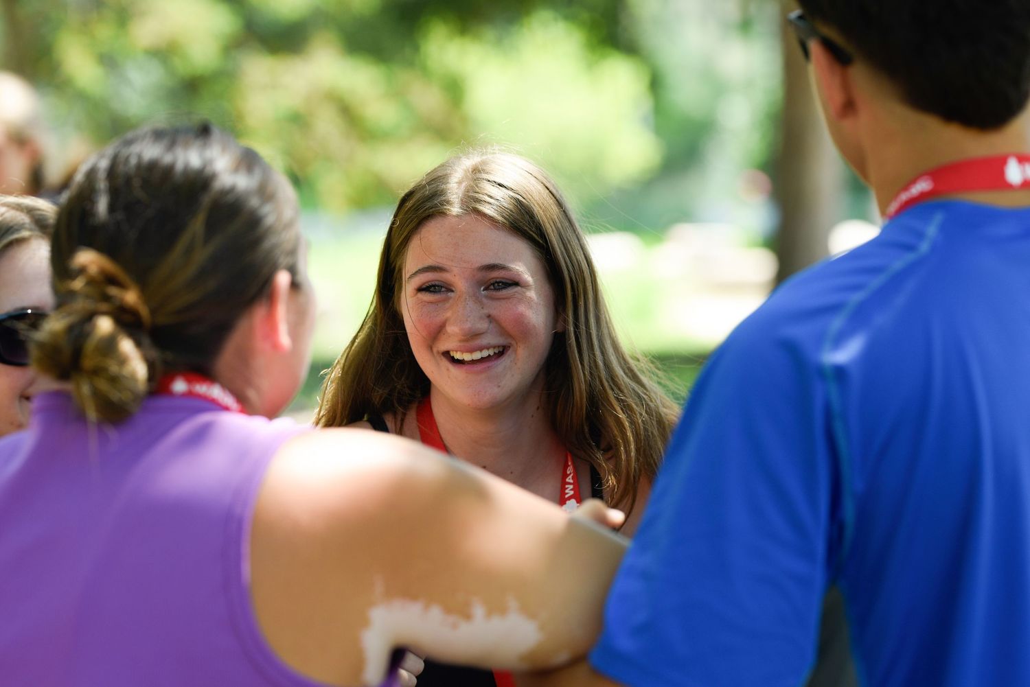 A smiling young woman in red engages in conversation outdoors on a sunny day.