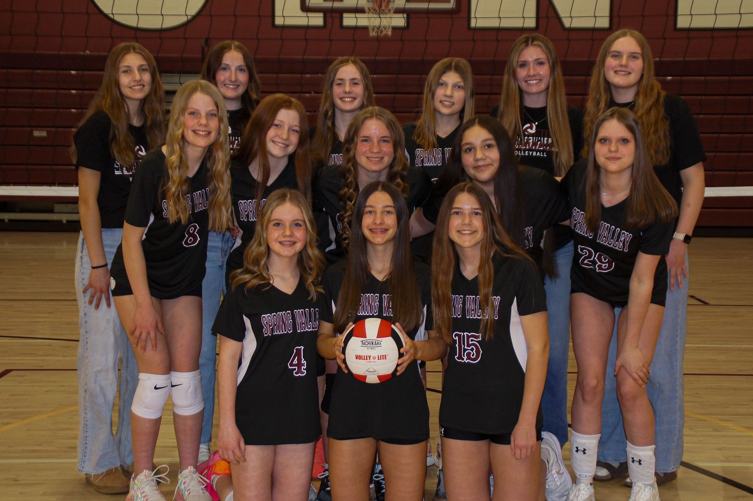 Spring Valley Cardinals girls volleyball team posing together in black uniforms on court.