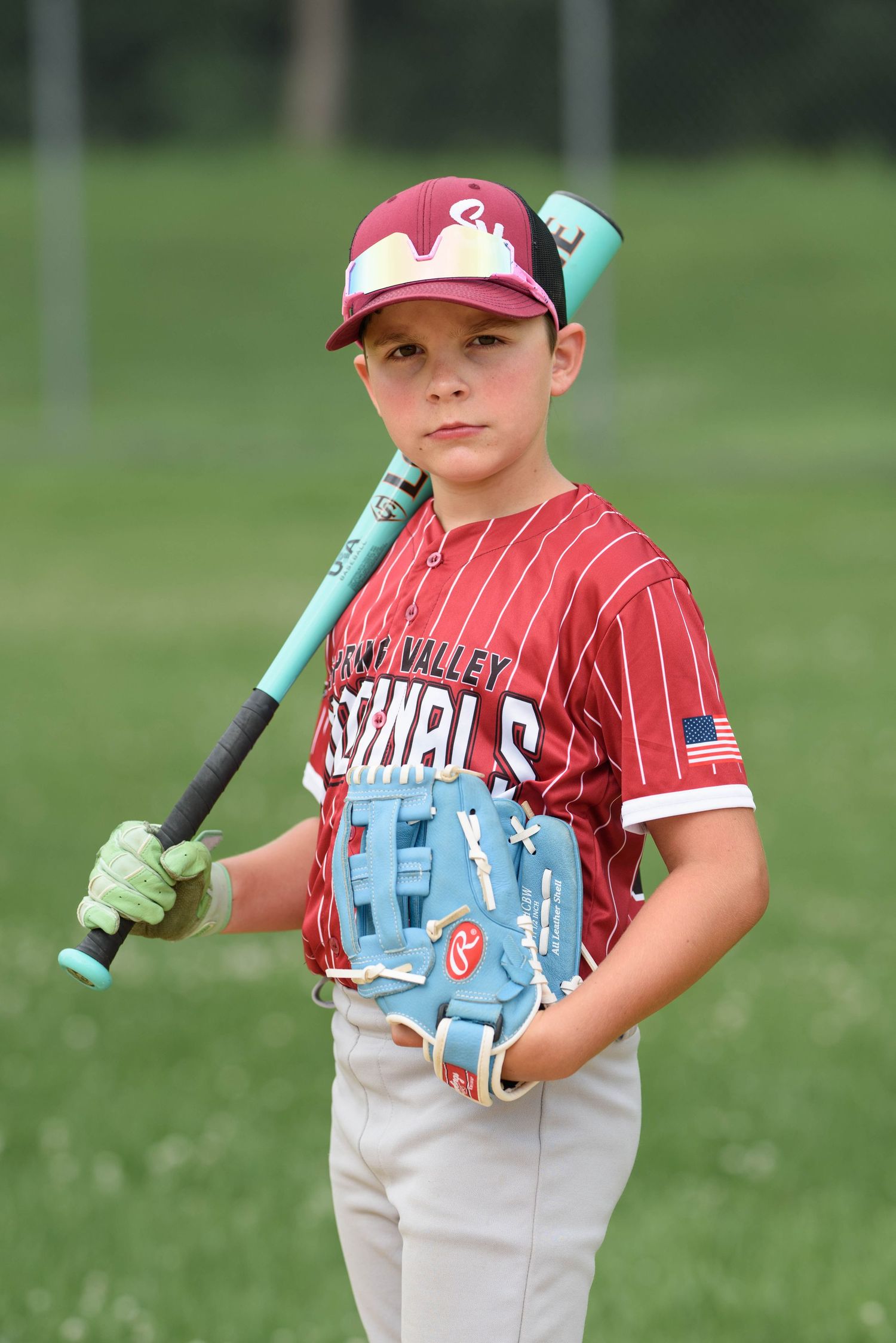 Young Spring Valley Cardinals baseball player posing with teal bat and blue glove in striped red uniform.