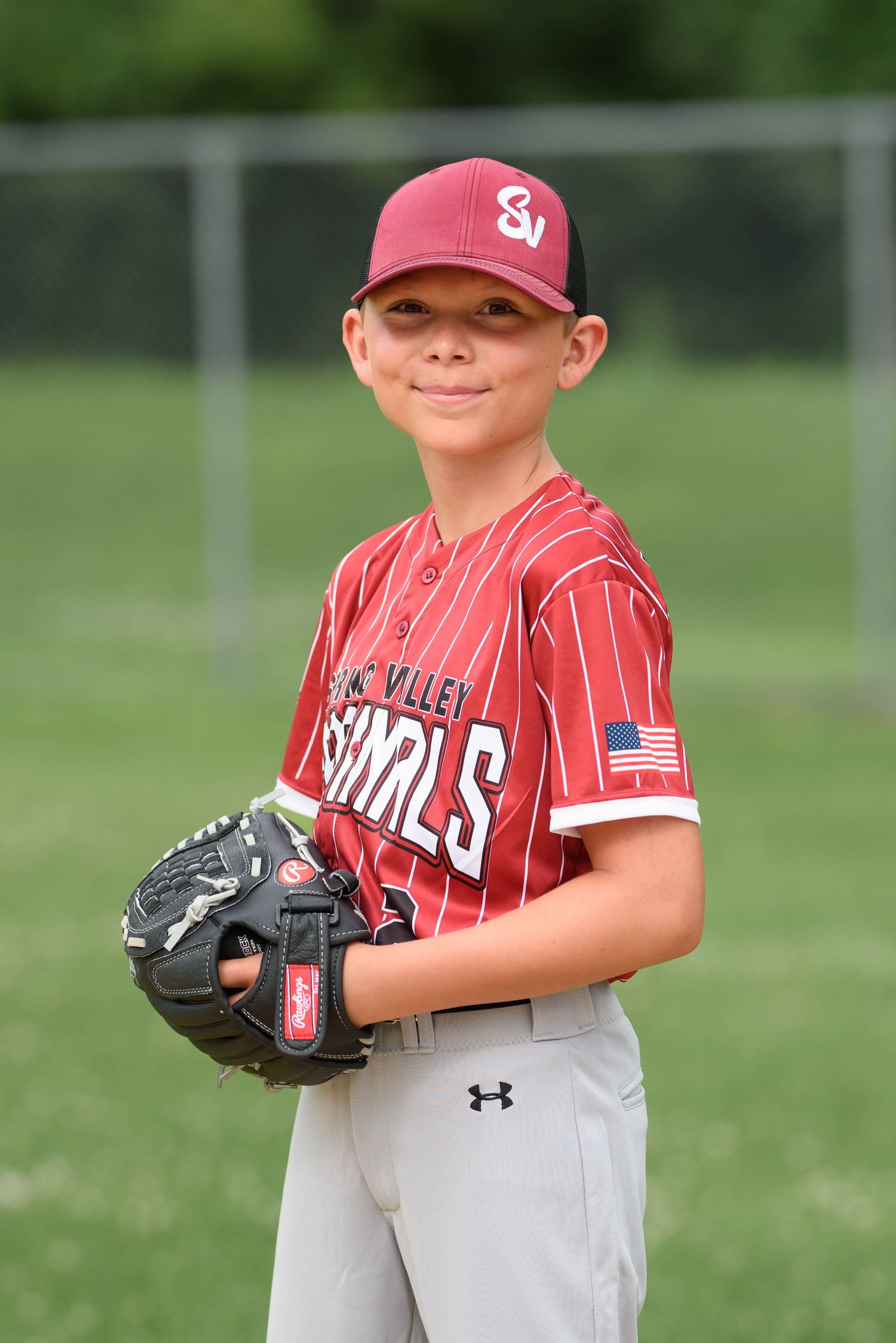Young baseball player in maroon SV Sharks uniform holding glove, posing for team photo on green field.