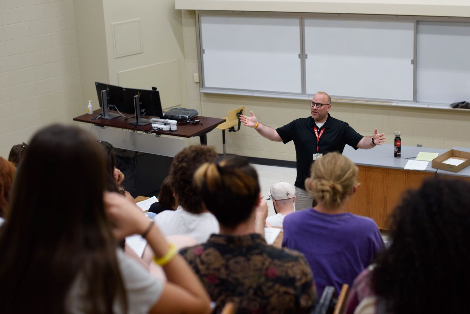 Professor gestures expressively while lecturing to a classroom full of attentive students in a university setting.