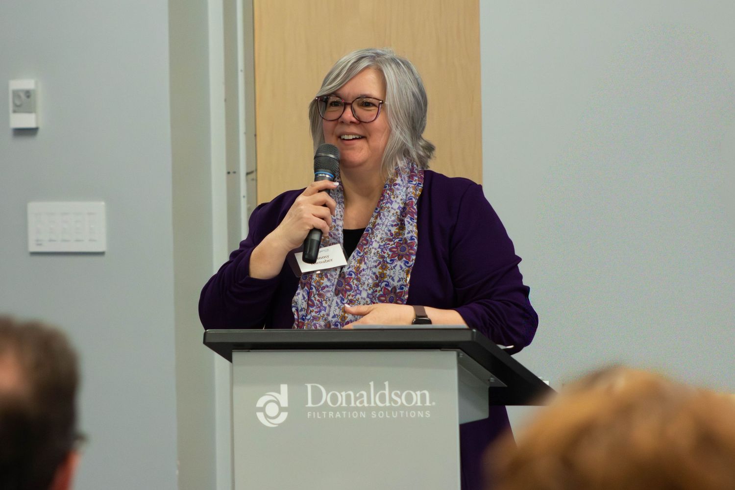 A woman in a purple blazer speaks at a Donaldson podium during a professional presentation event.