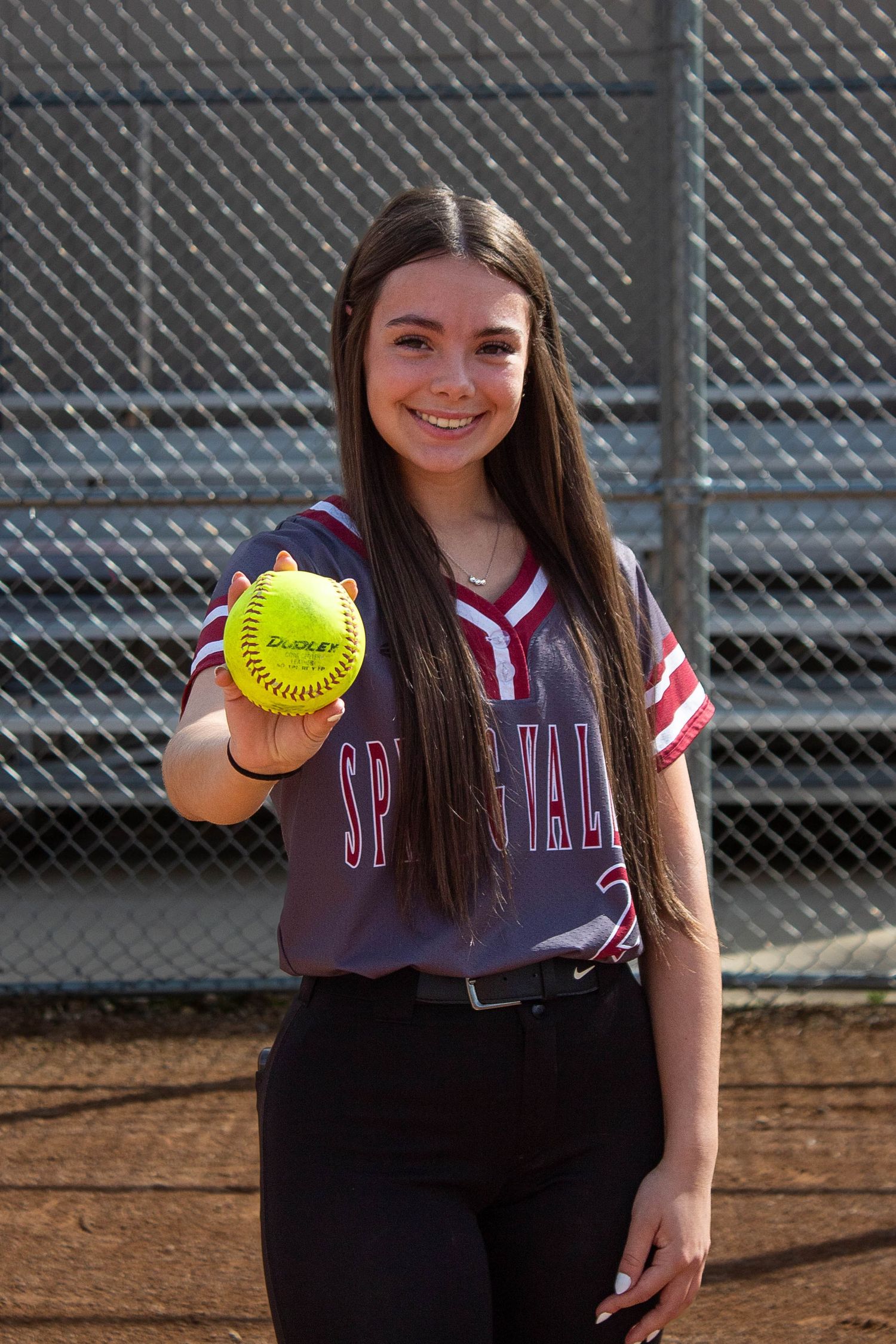 Spring Valley softball player extends a yellow Dudley softball toward the camera on the dirt field.