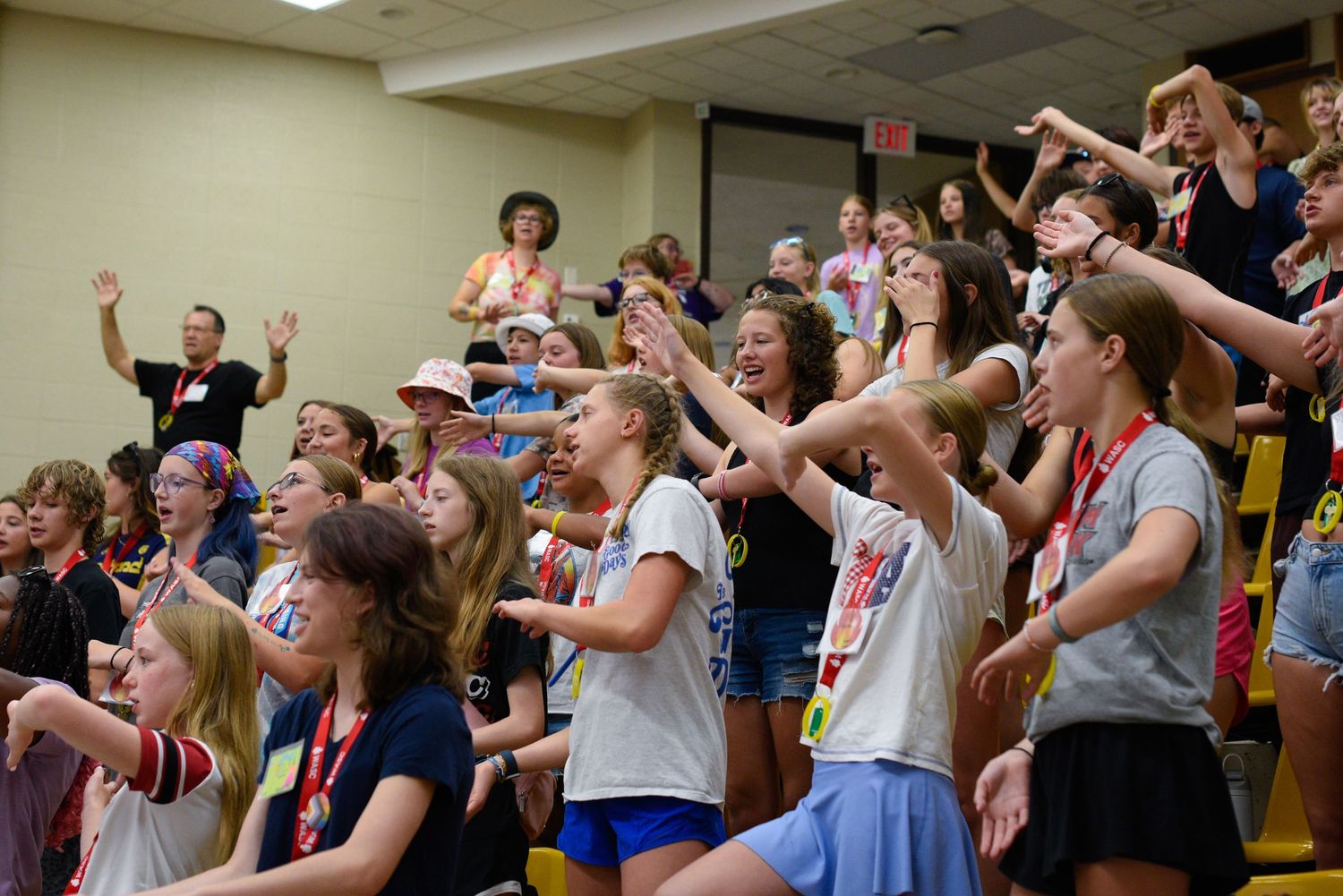 Excited girls cheering and dancing together at a youth camp event in an auditorium setting.