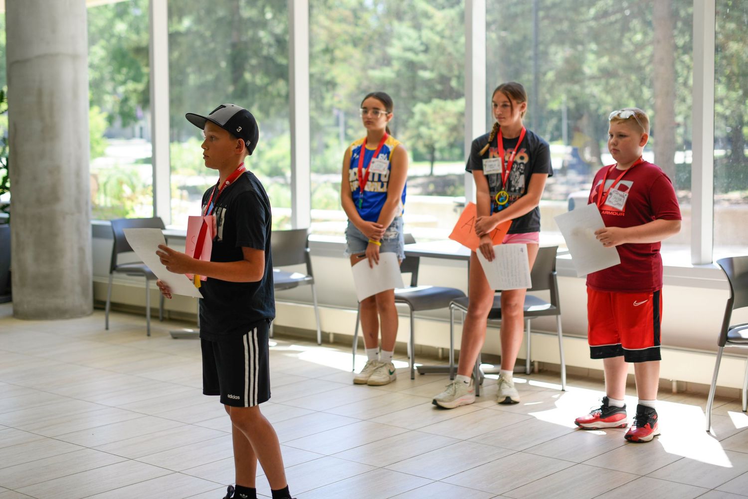 Four young athletes stand indoors holding awards at a youth sports recognition ceremony.