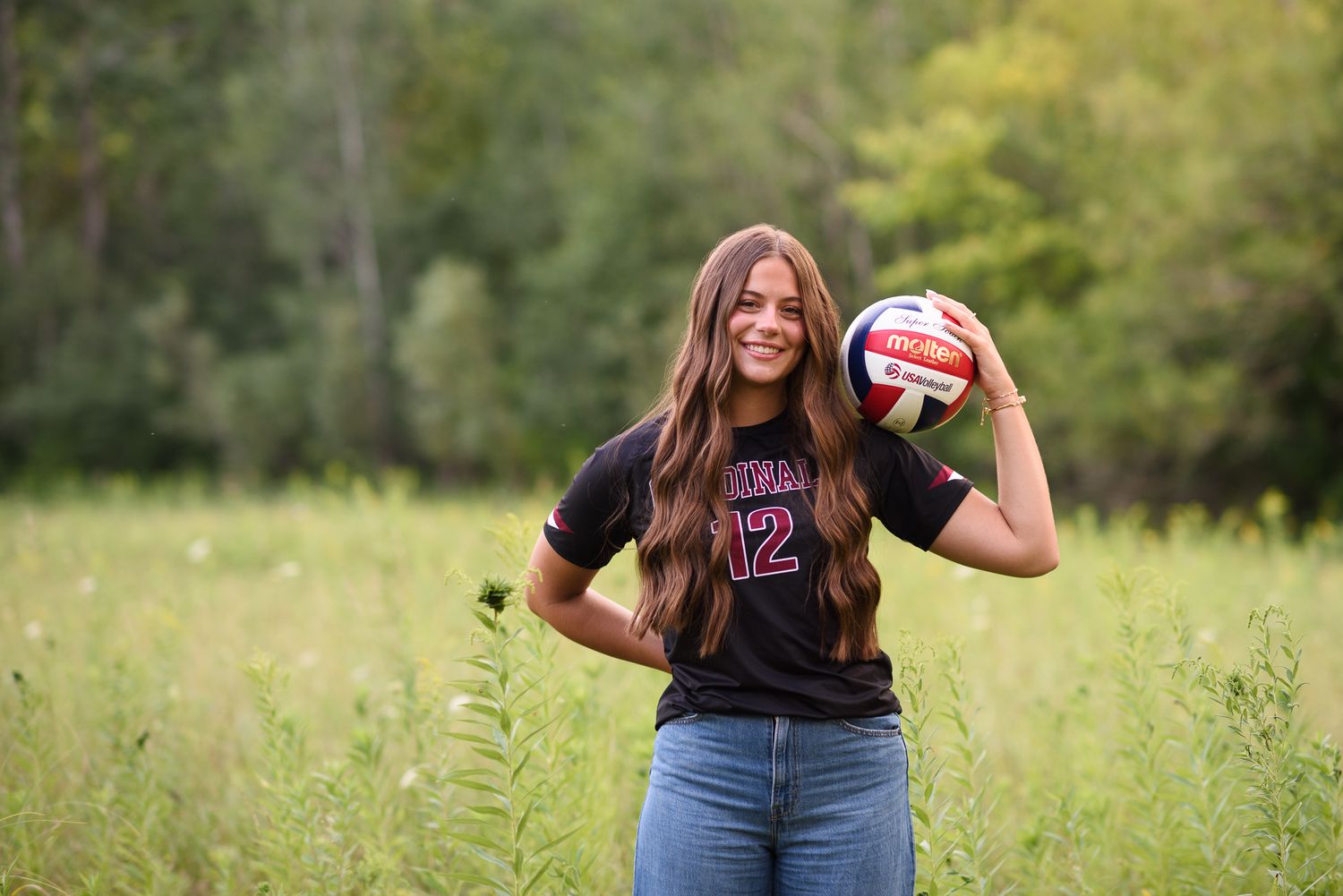 Teen girl in Cardinals volleyball jersey #12 holding a volleyball in a green field.