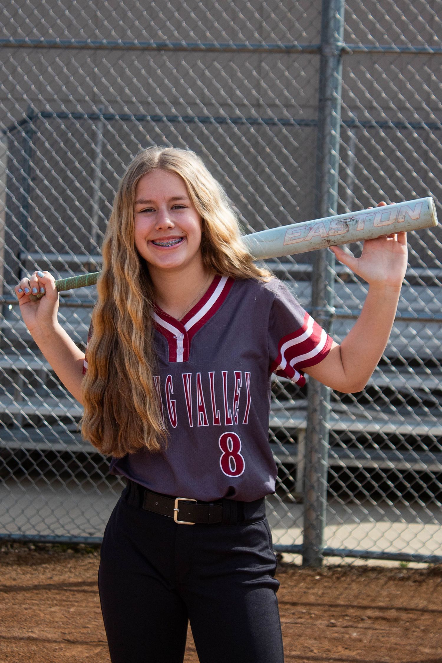 Smiling softball player number 8 poses with bat on shoulder in Spring Valley uniform.