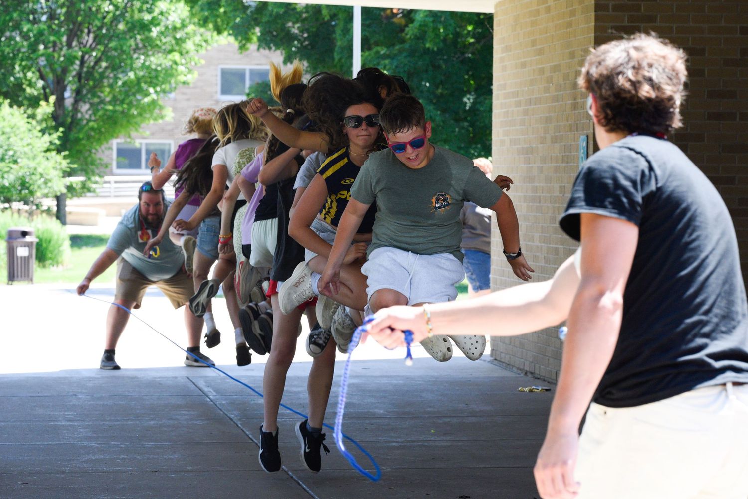 Group of teens jumping rope together outdoors on a sunny day near a brick building.