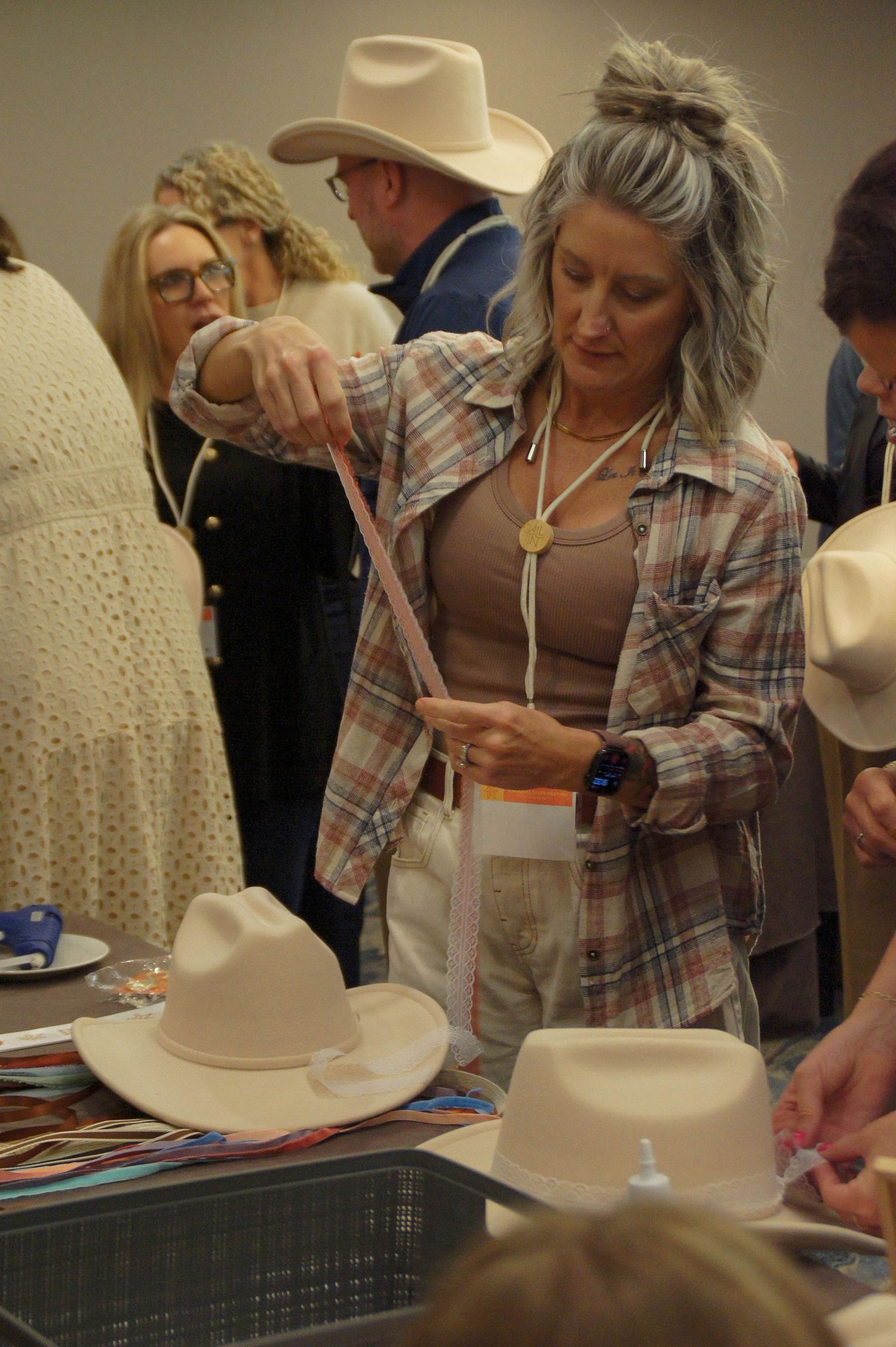 Woman customizing a felt cowboy hat with a decorative band at a trade event.