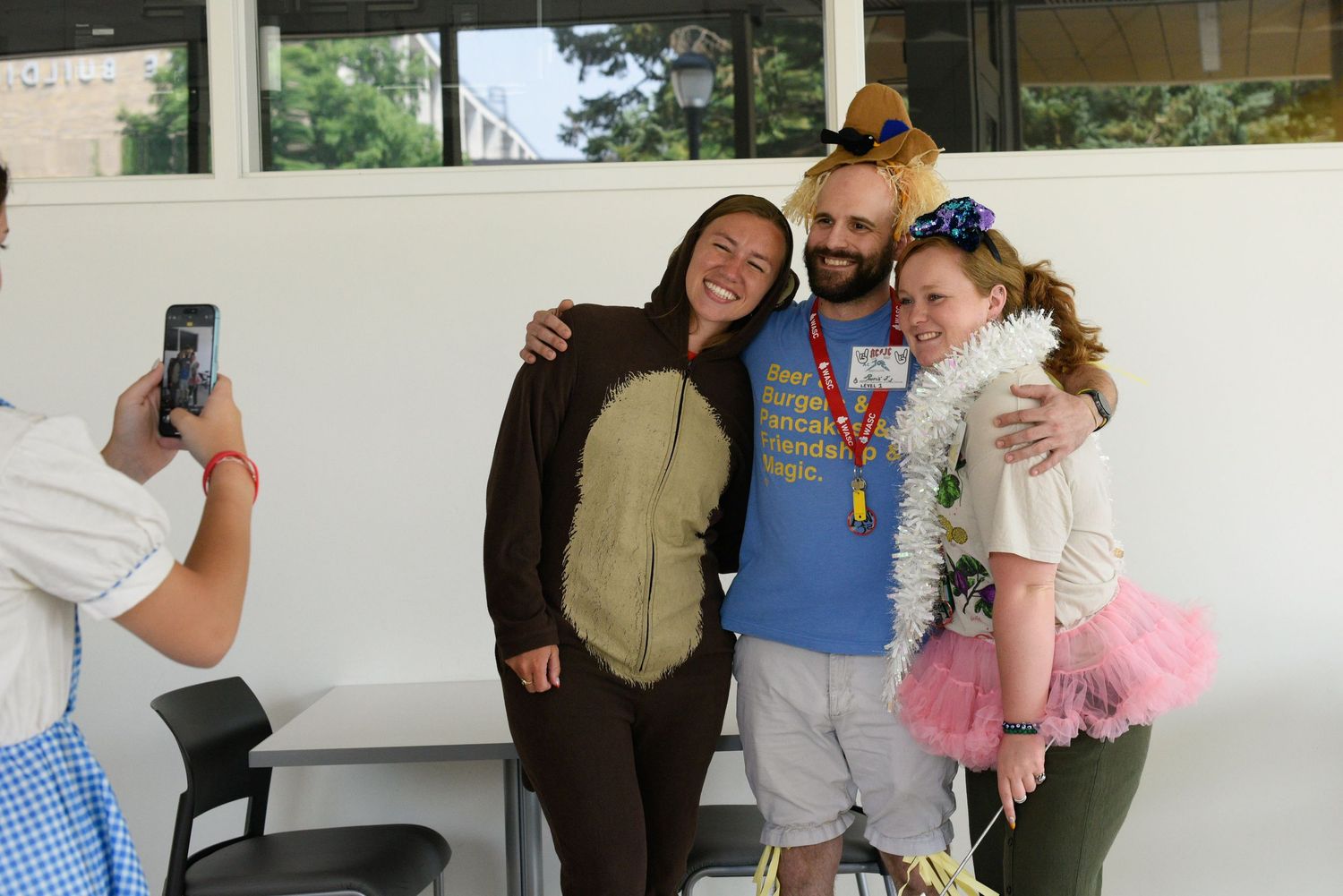 Group of adults in fun costumes posing for a photo indoors, smiling and celebrating at a festive event.