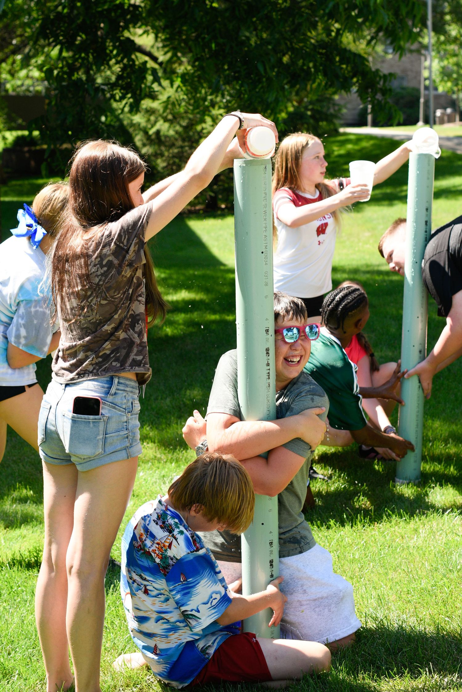 teens playing outdoor team building game on grass around tall poles on sunny day.