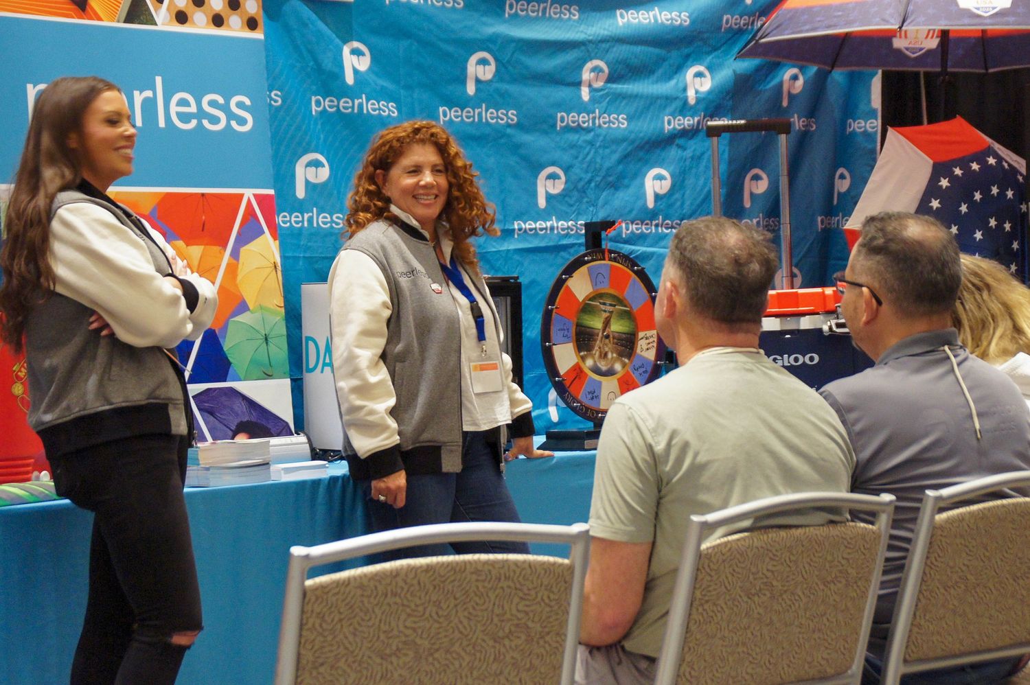 Two women present at a Peerless trade show booth with a prize wheel display.