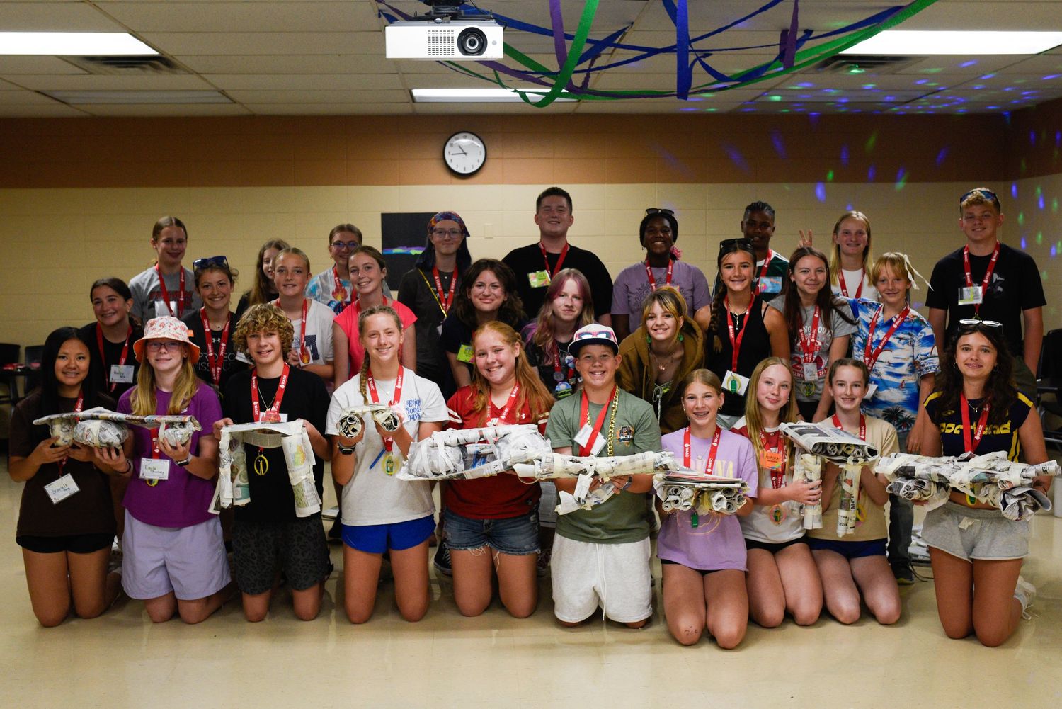 large group of smiling students holding model planes indoors at school STEM event.