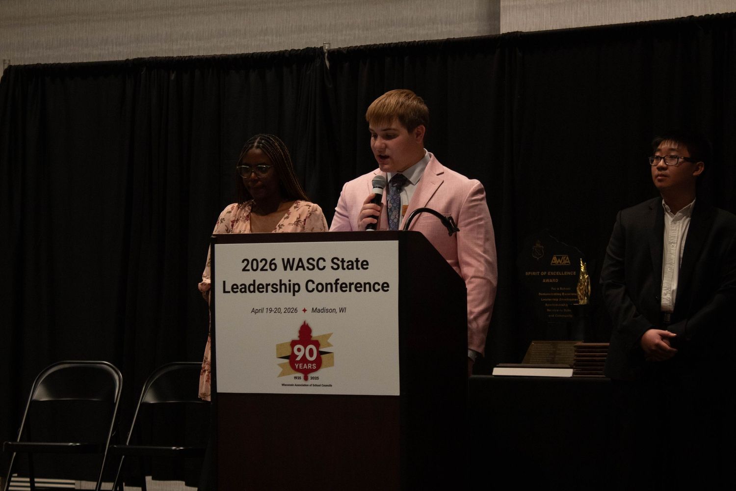 Three students present at the 2026 WASC State Leadership Conference podium on stage.