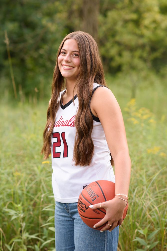 Teen girl in Cardinals #21 jersey holding a Spalding basketball, smiling outdoors in a green field.