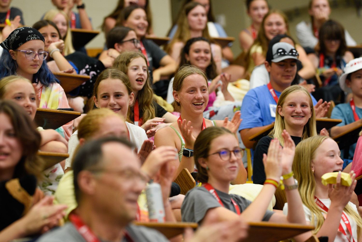Excited crowd of young girls and adults smiling and waving in auditorium seating at a lively group event.