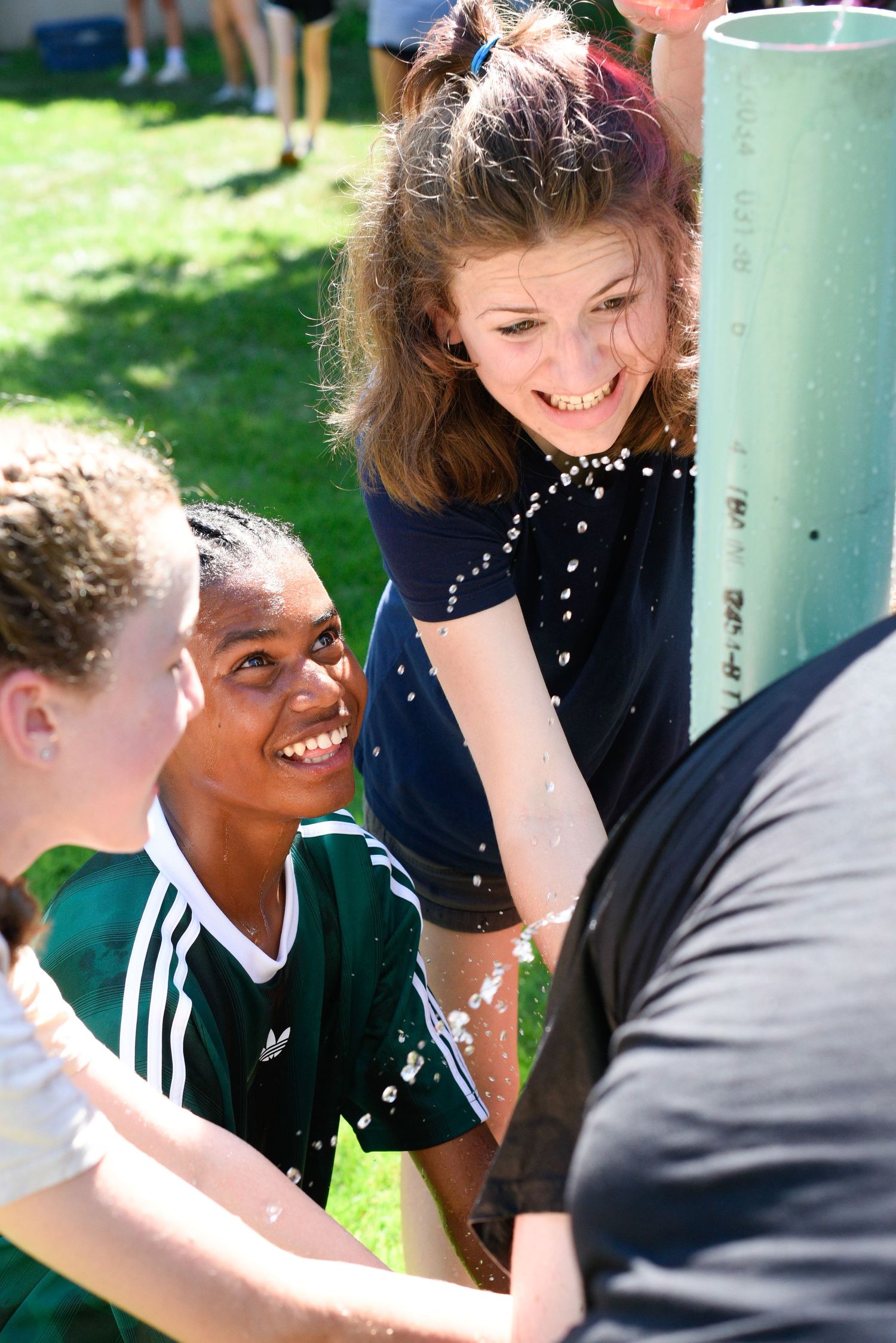 Group of smiling teens collaborating on outdoor water activity game on sunny day.