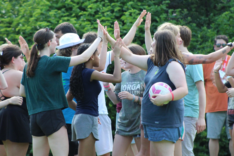 Students form a line with raised arms in a high-five chain during an outdoor team-building activity at dusk.