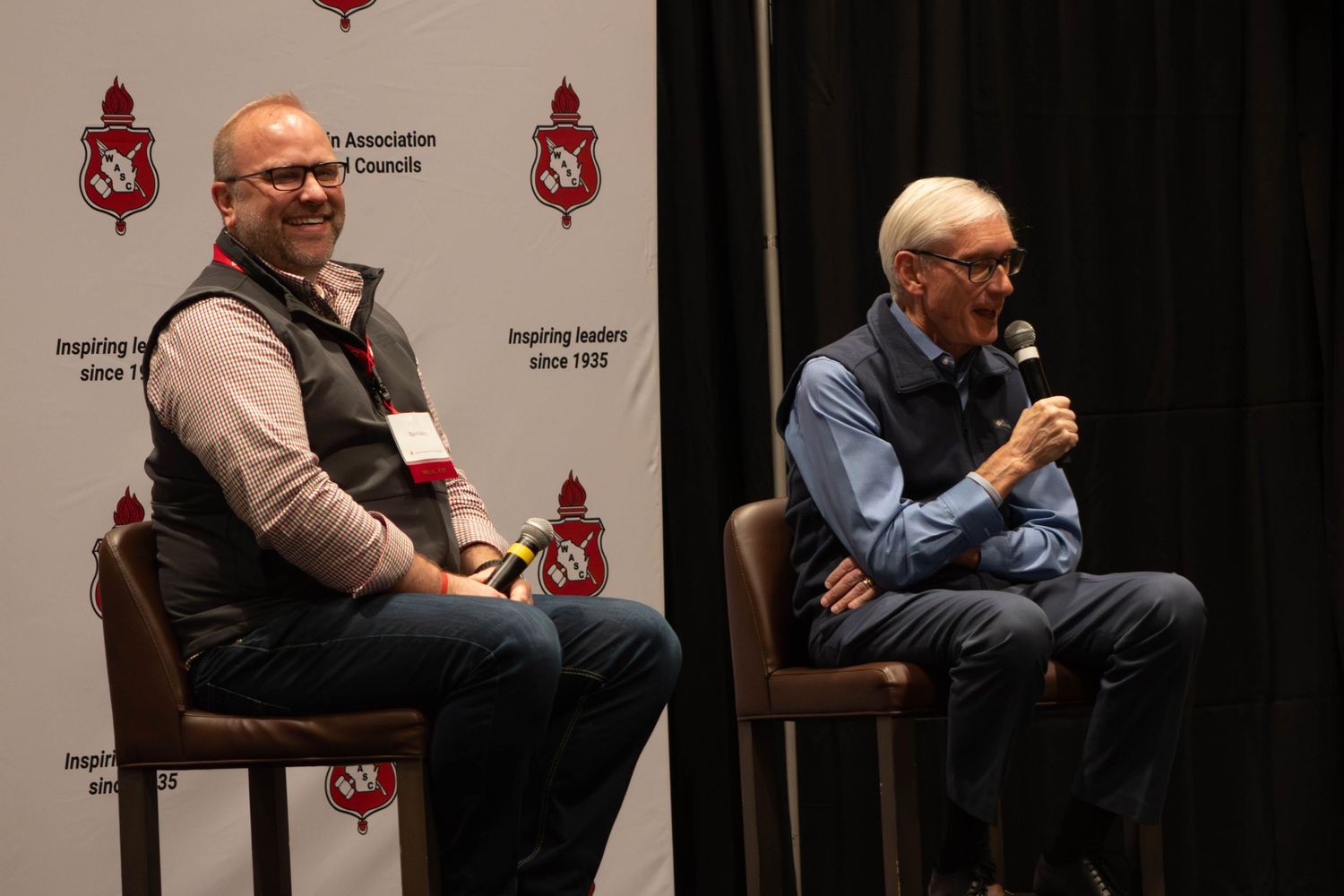Two men seated on stage during a panel discussion at a leadership conference.