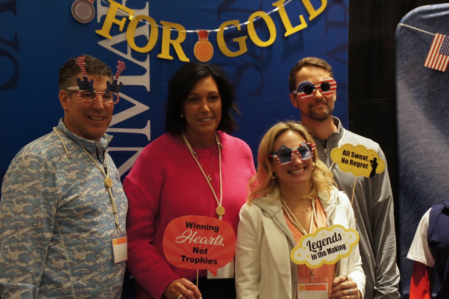 Four people posing at a Go for Gold themed trade show booth with fun props.