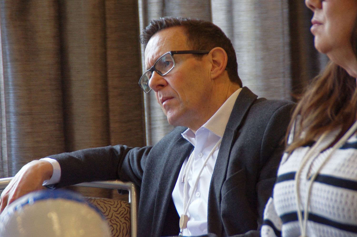 Professional man in blazer and glasses listens attentively during business conference session.
