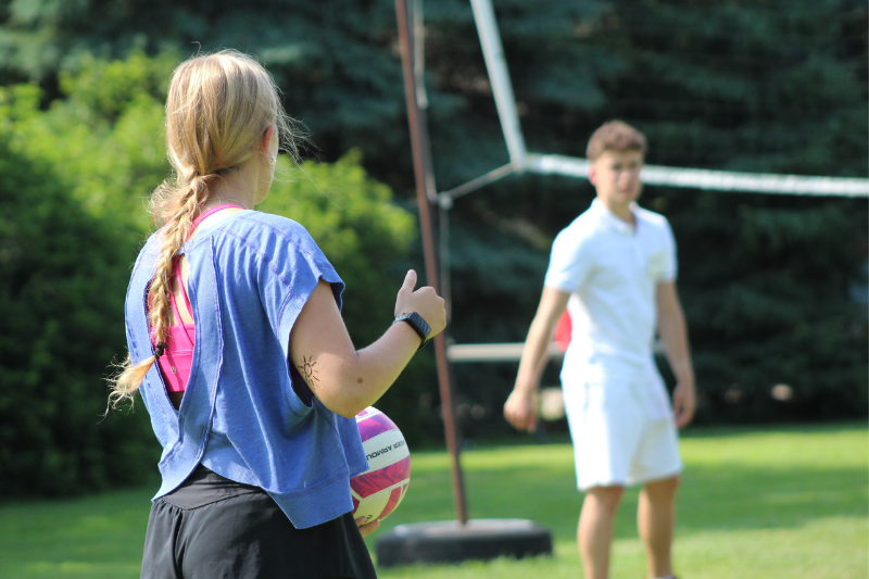 A girl with a braided ponytail holds a volleyball while playing outdoor volleyball on a grassy field.