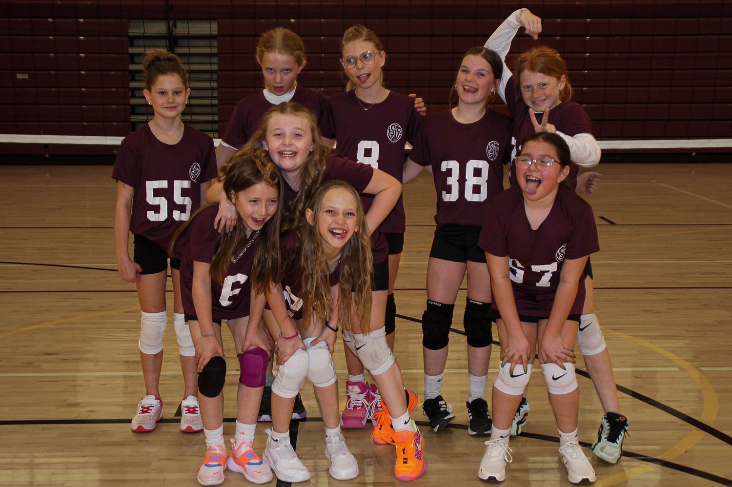 Young girls volleyball team in maroon uniforms posing together on indoor court smiling.