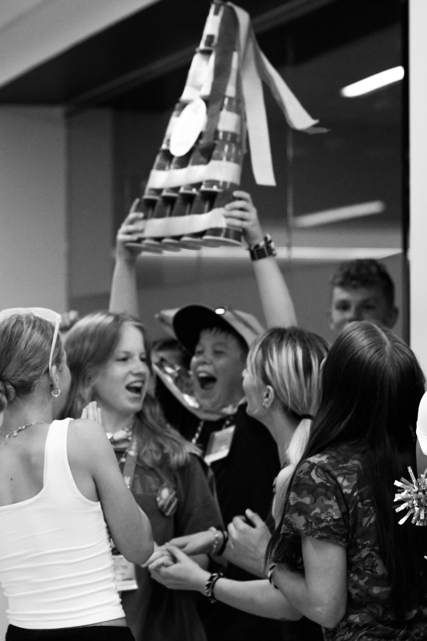 Group of excited kids celebrating at a party with a pyramid-shaped trophy held high in black and white photo.