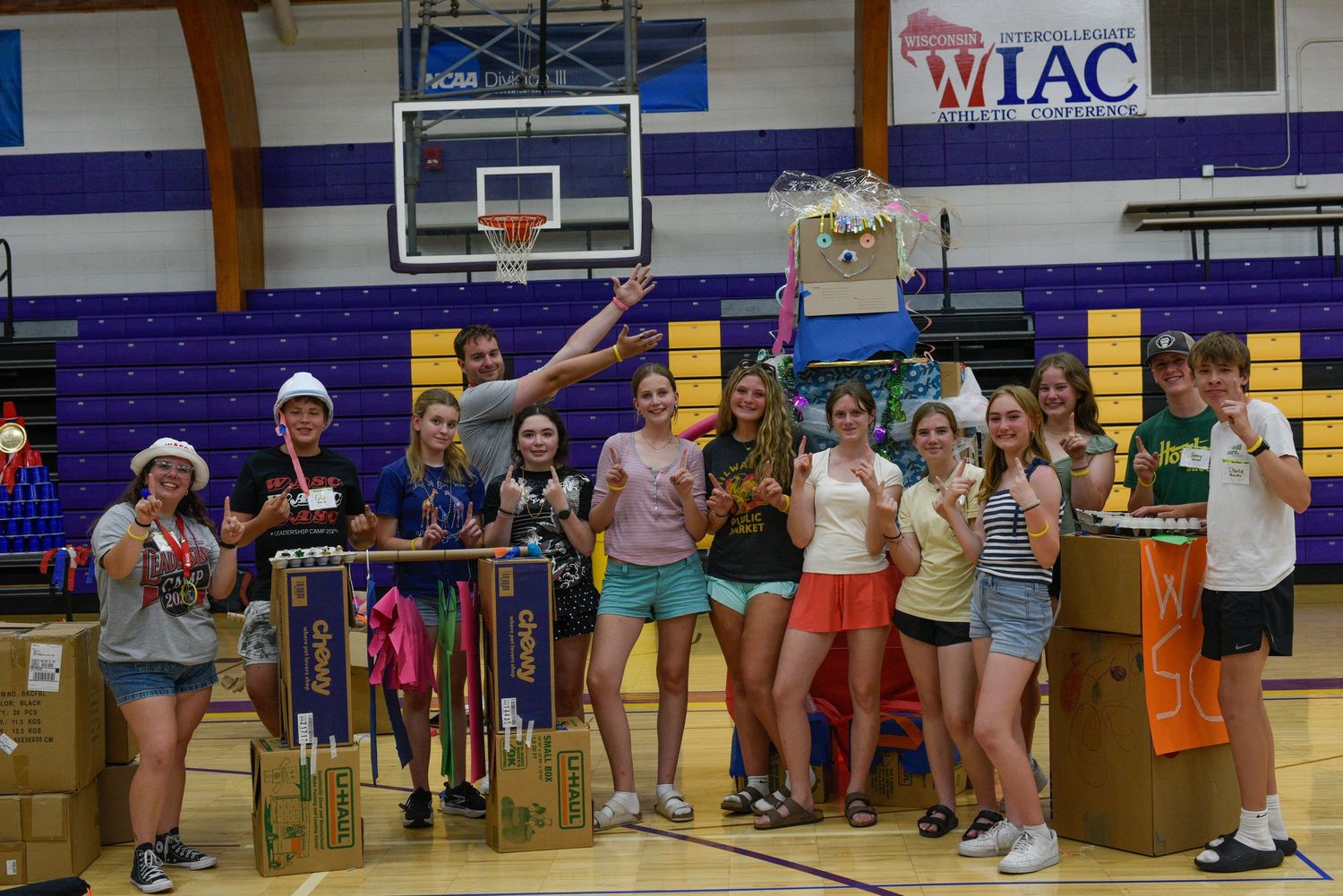 Students celebrate in a gym with trophies and projects at a WIAC academic competition event.