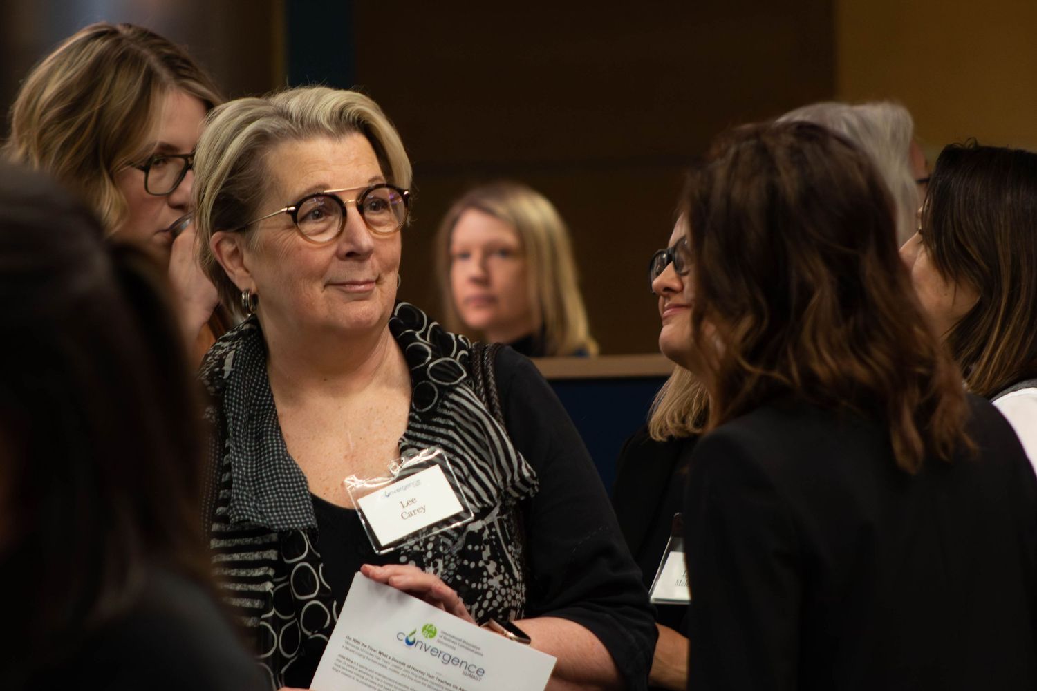 Professional women networking at a business conference event, smiling and engaging in conversation.