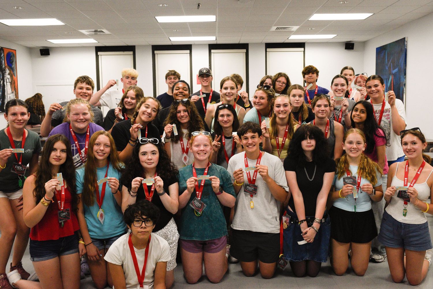 Large group of smiling teens holding medals together in a classroom, celebrating an achievement at a youth event.