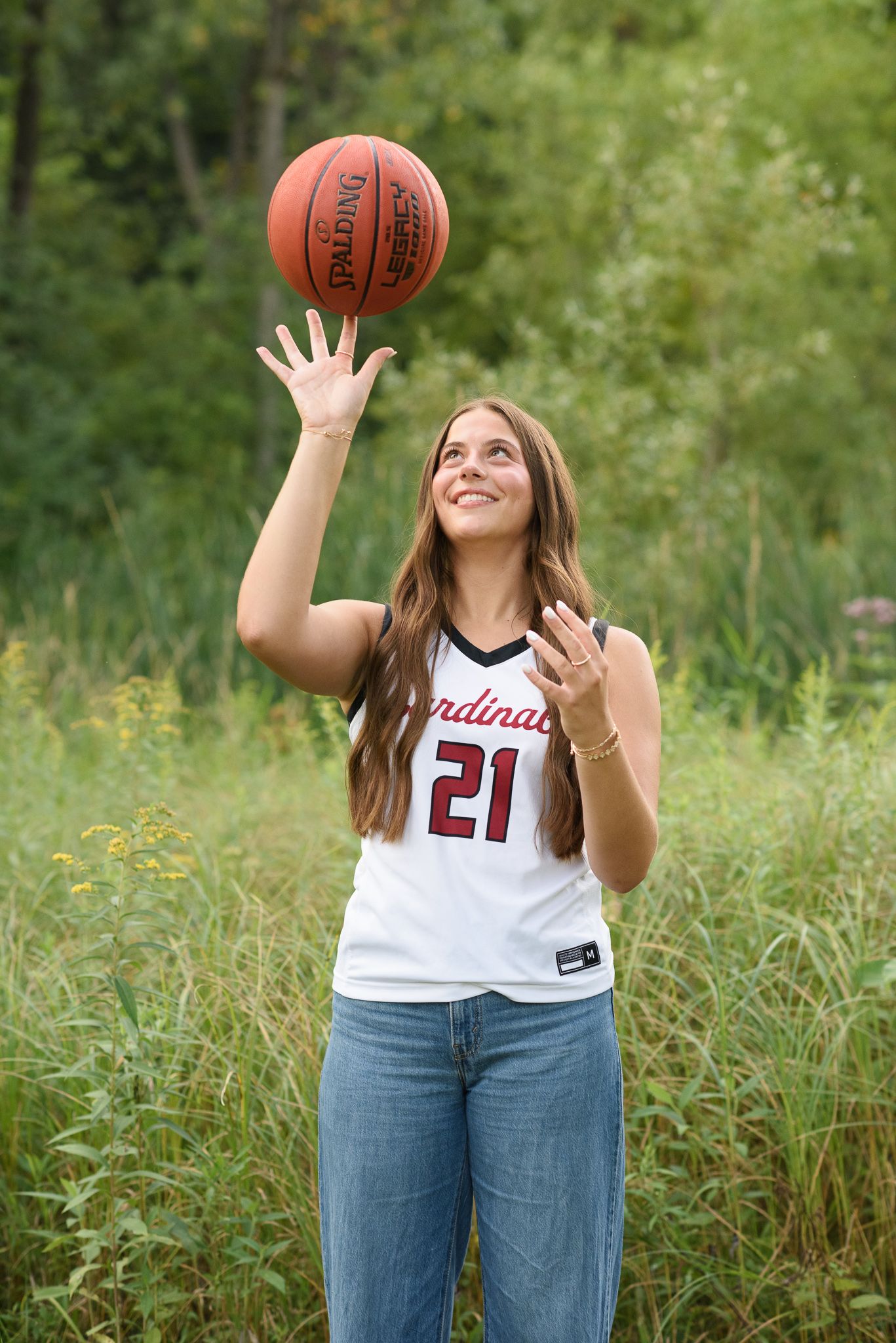 Young female basketball player in Cardinals #21 jersey tossing a Spalding ball in a lush green field.