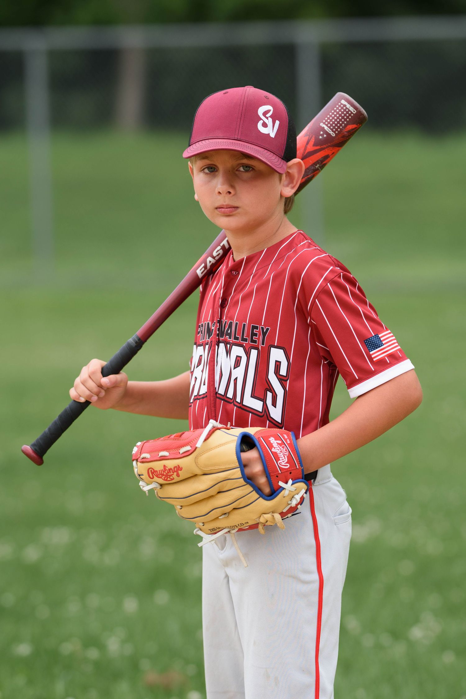 Young baseball player in red Cardinals uniform holding bat over shoulder with glove, posing for team photo.