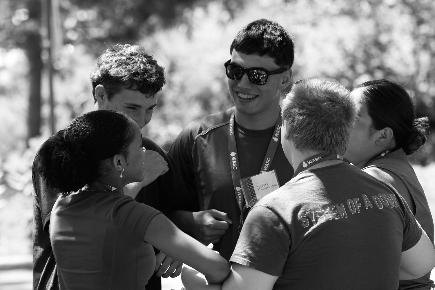 Black and white photo of a diverse group of young people smiling and gathered together outdoors in a park setting.