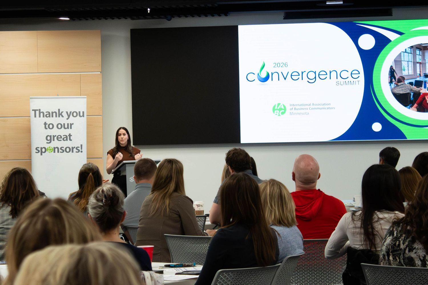 Speaker presents at Convergence conference event with audience seated in modern venue with sponsor banner displayed.