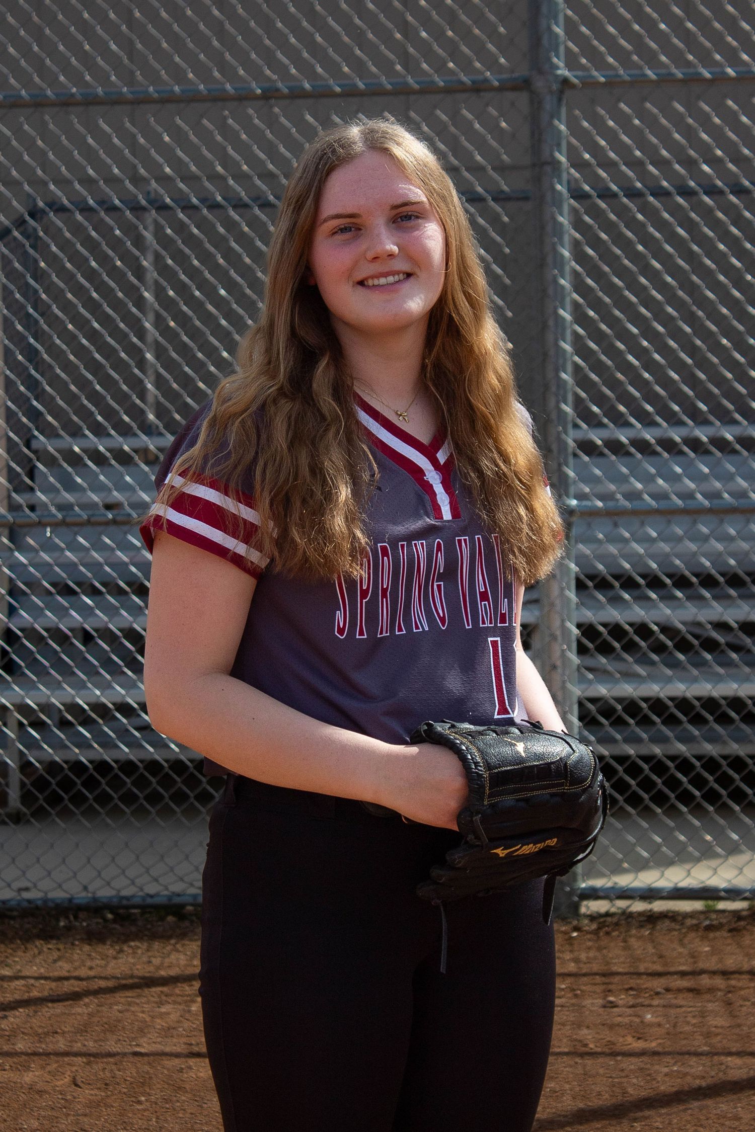 Spring Valley softball player #1 smiles holding a glove in a maroon Spring Valley jersey on the field.