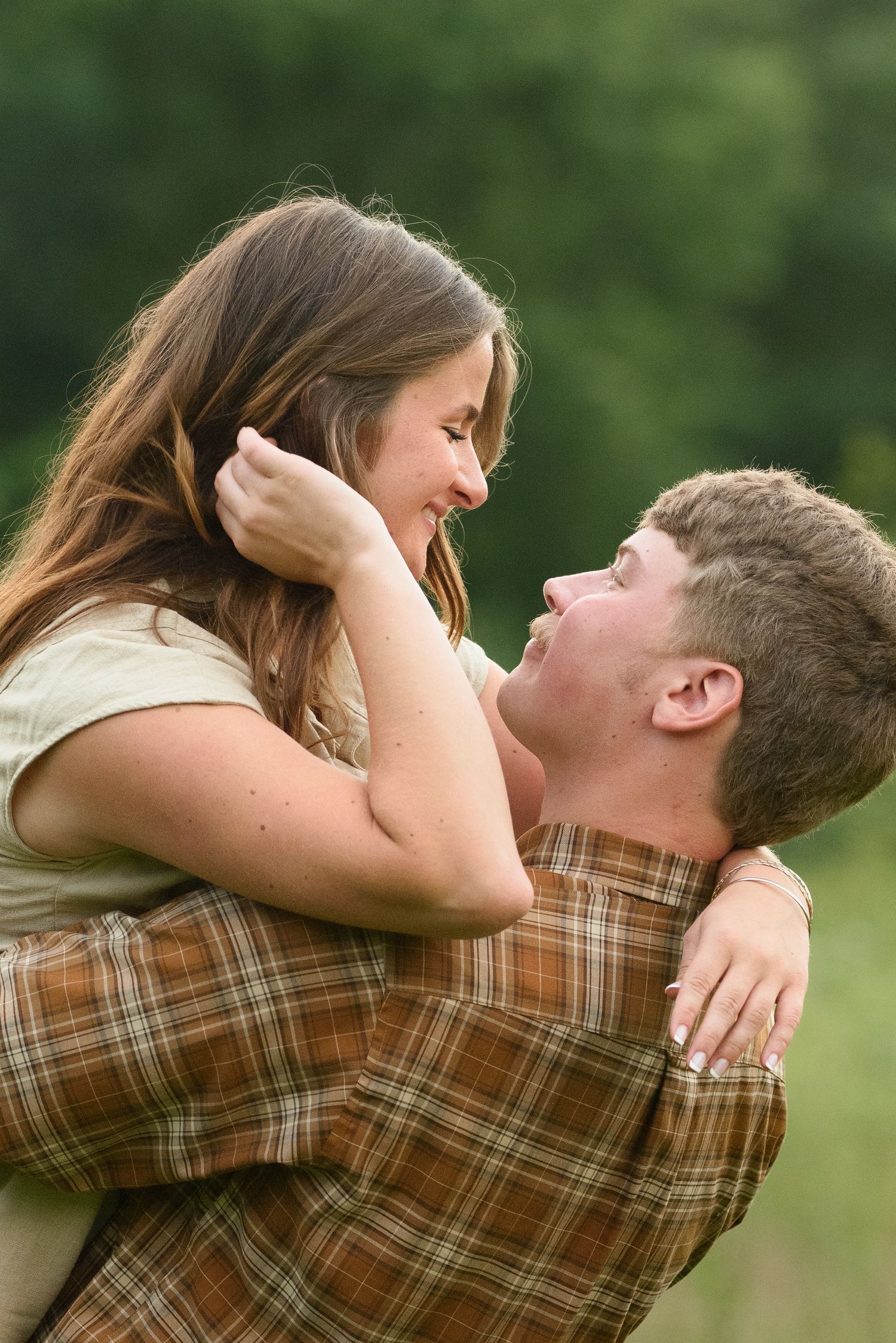 A joyful couple shares a romantic moment as the man lifts the woman in a green outdoor setting.