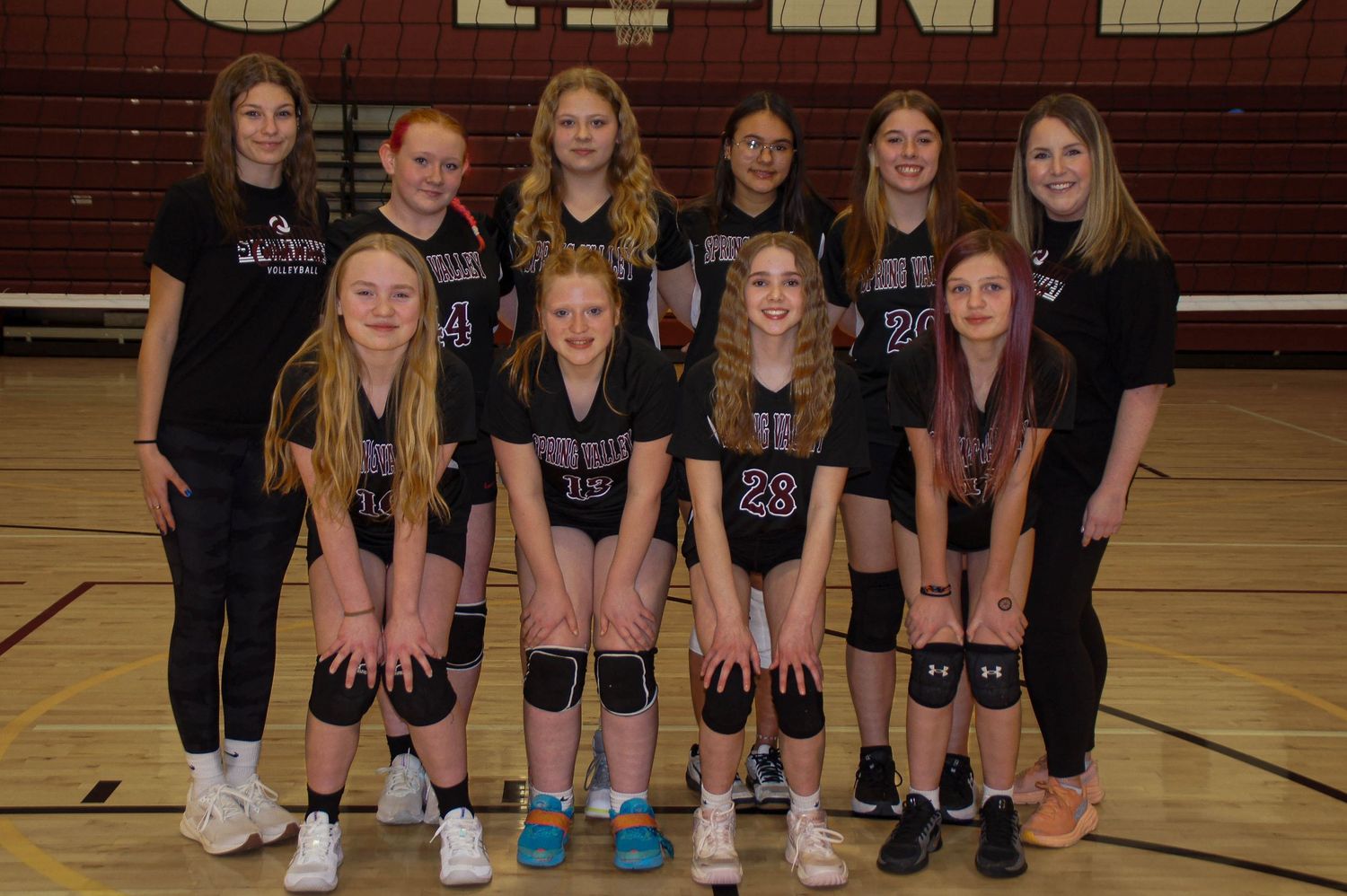 Youth girls volleyball team in black Spring Valley uniforms posing on indoor court.