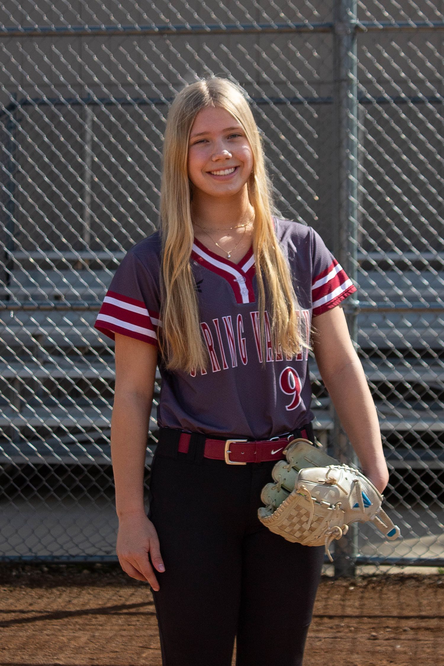 Blonde softball player in Spring Valley number 9 jersey holds glove on dirt field.
