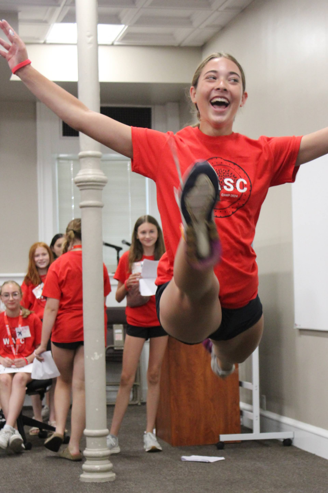 Joyful student in red SC shirt leaps high in the air during an energetic indoor dance or cheer activity.