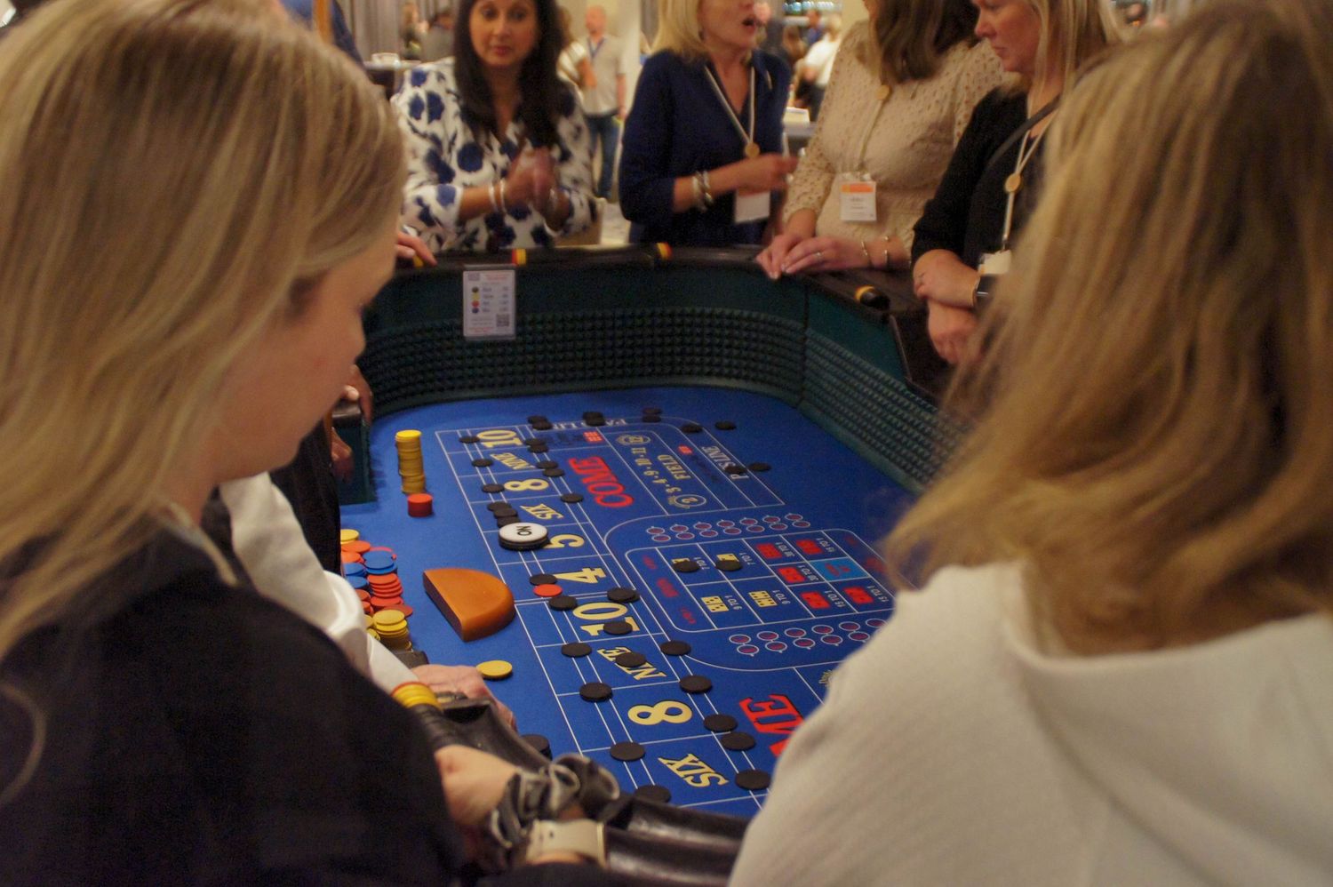 Women gathered around a blue roulette table at a casino night event.
