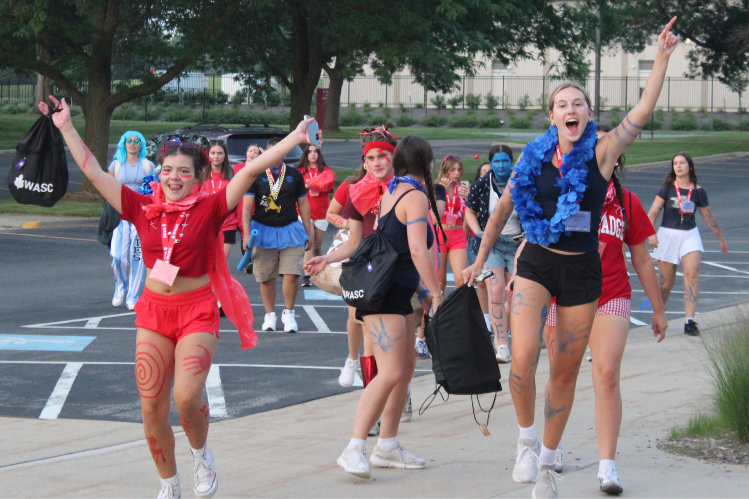 Energetic students in red and blue costumes cheer and run during a lively outdoor campus activity event.