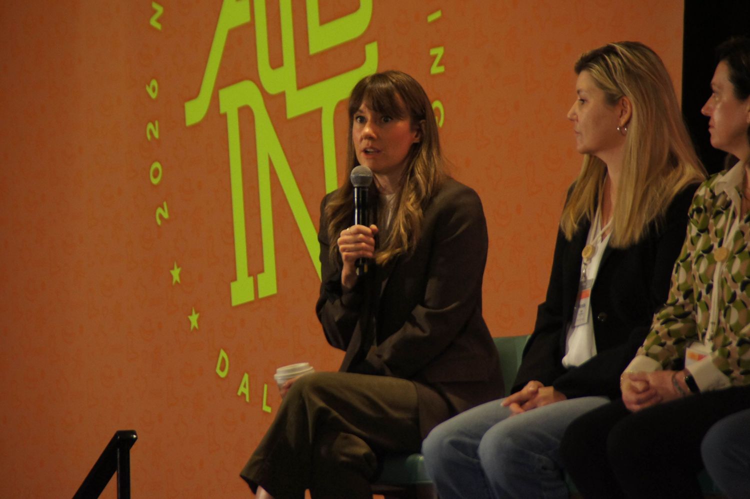 Woman in dark outfit speaks at an All In NSM 26 Dallas conference panel event.