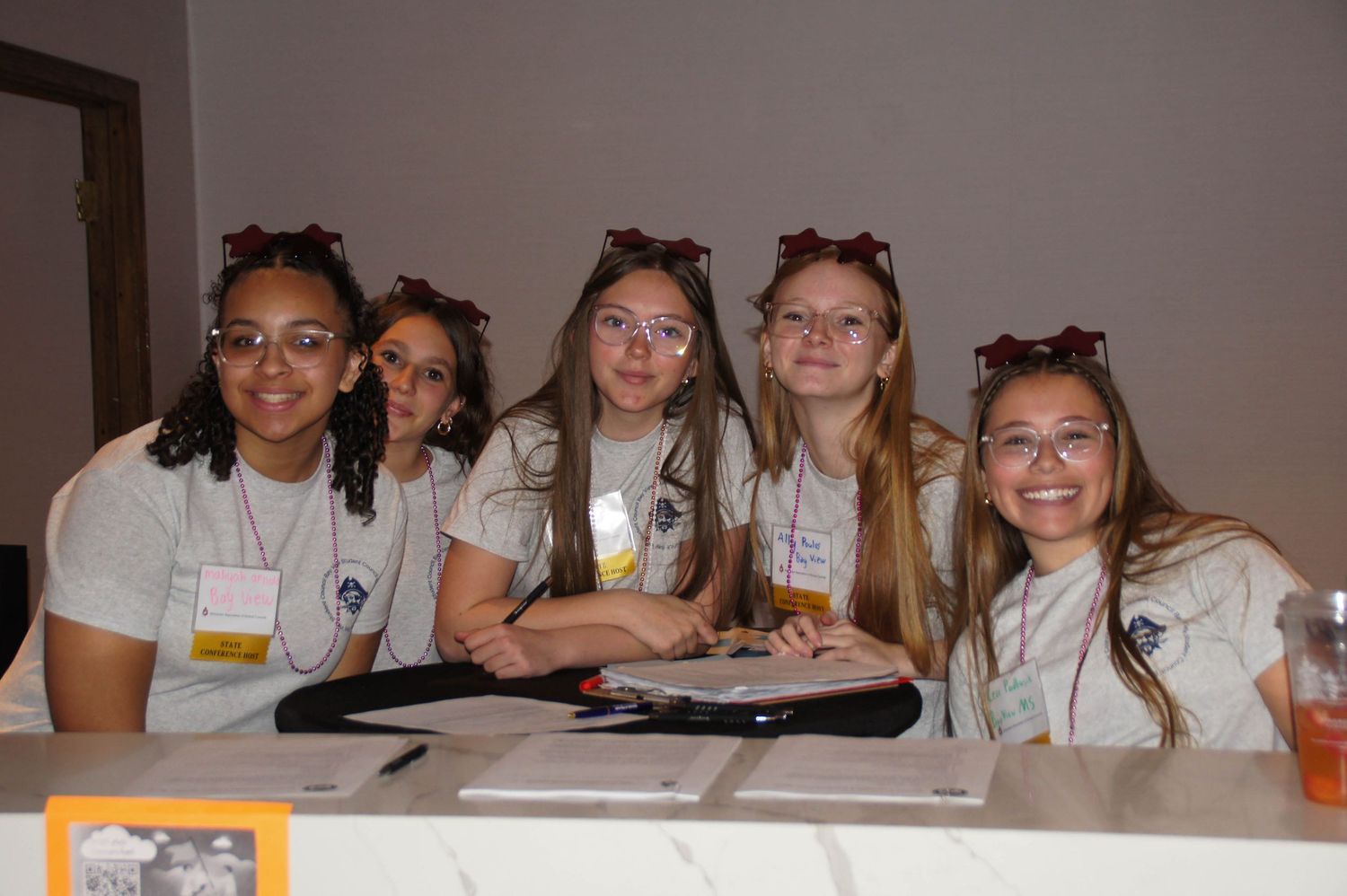 Five smiling students seated at a table during a school leadership conference.