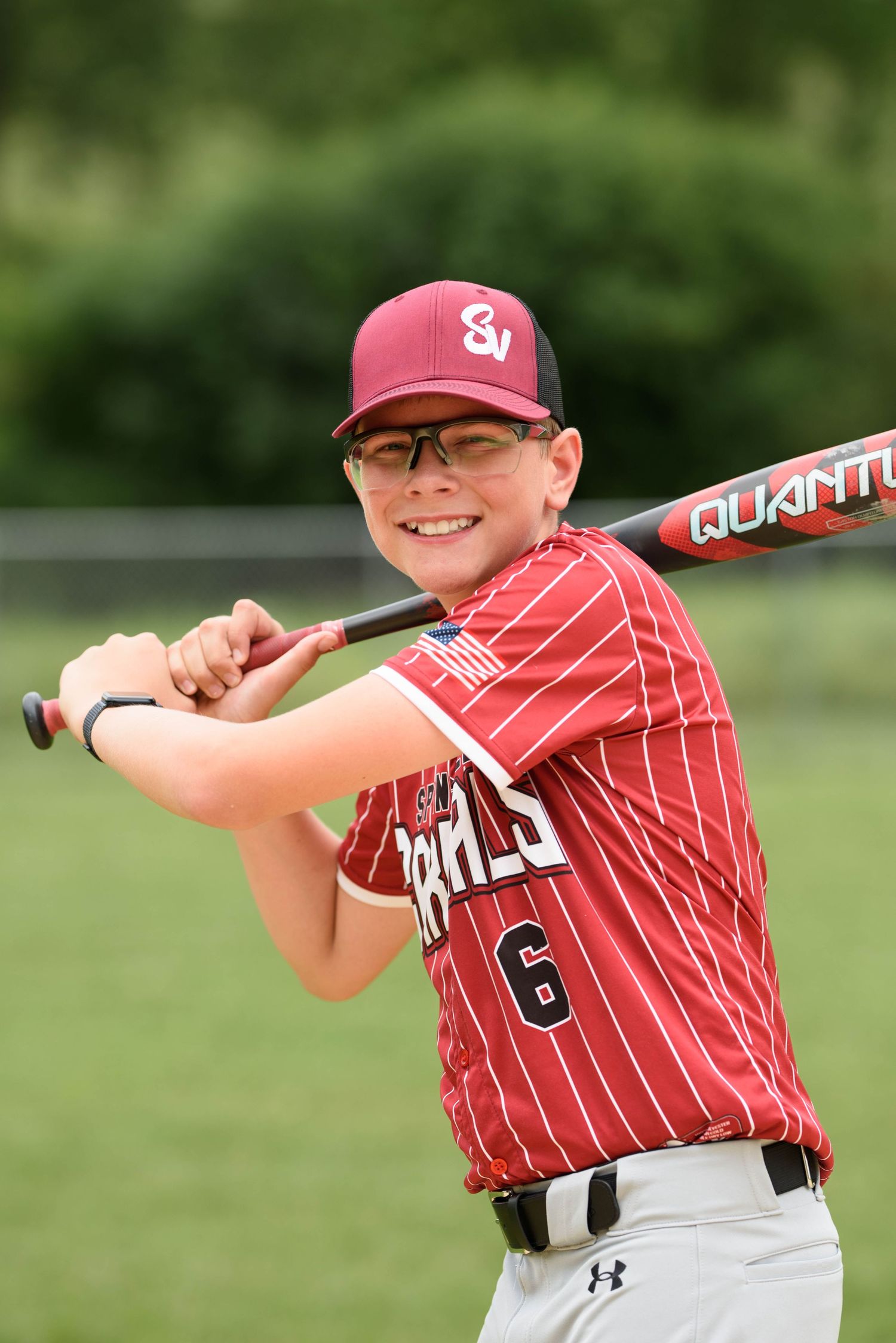 Young baseball player #6 in red pinstripe Cardinals uniform poses in batting stance holding Quantum bat outdoors.