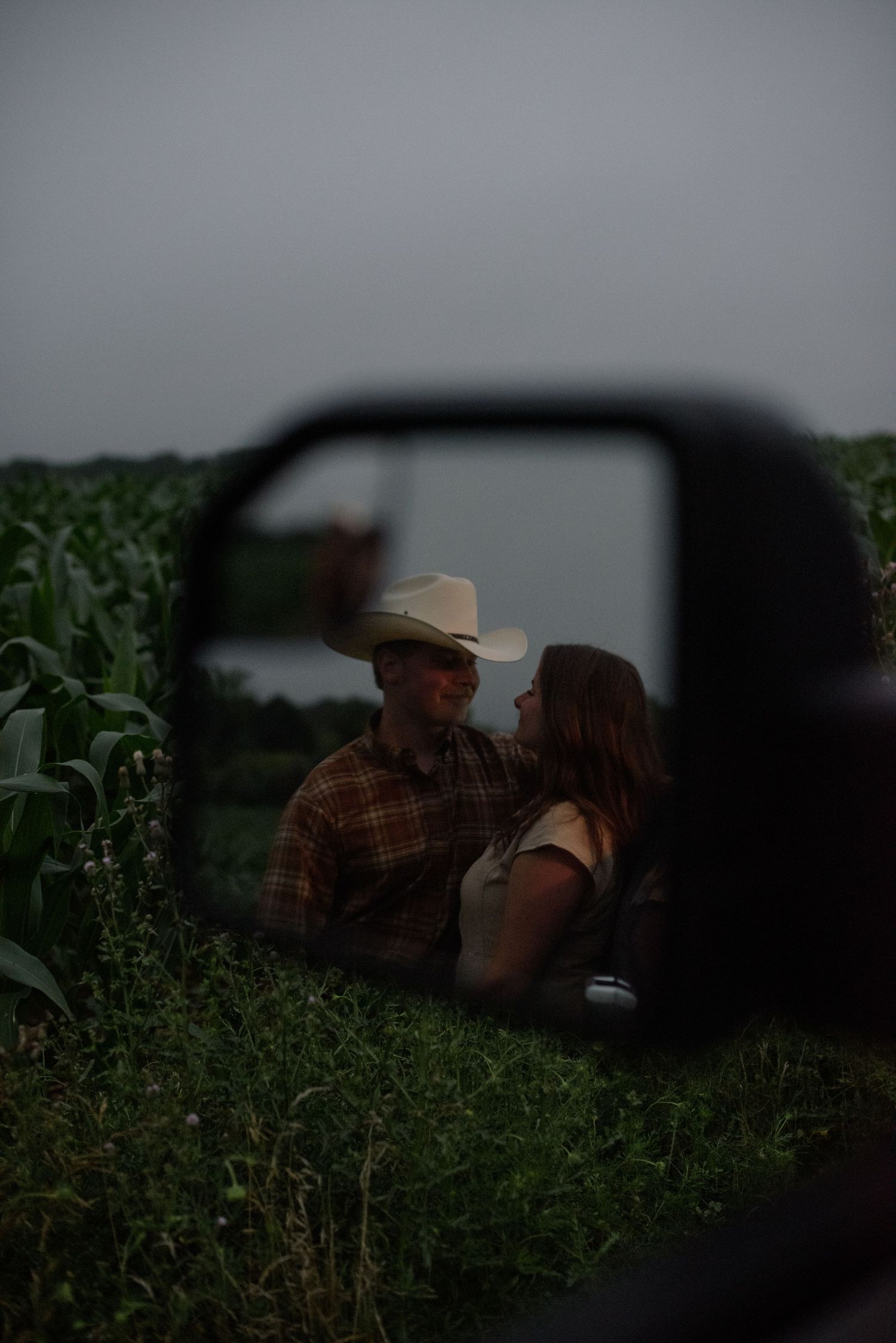 A couple shares a romantic moment in a cornfield, reflected in a truck side mirror.