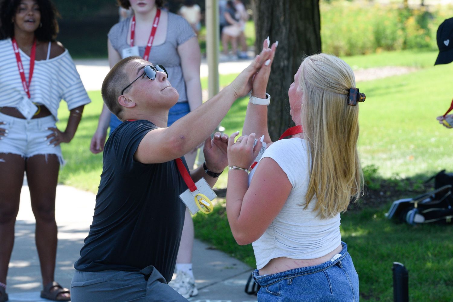 Two students high-five outdoors during a sunny campus event, with peers gathered in the background.