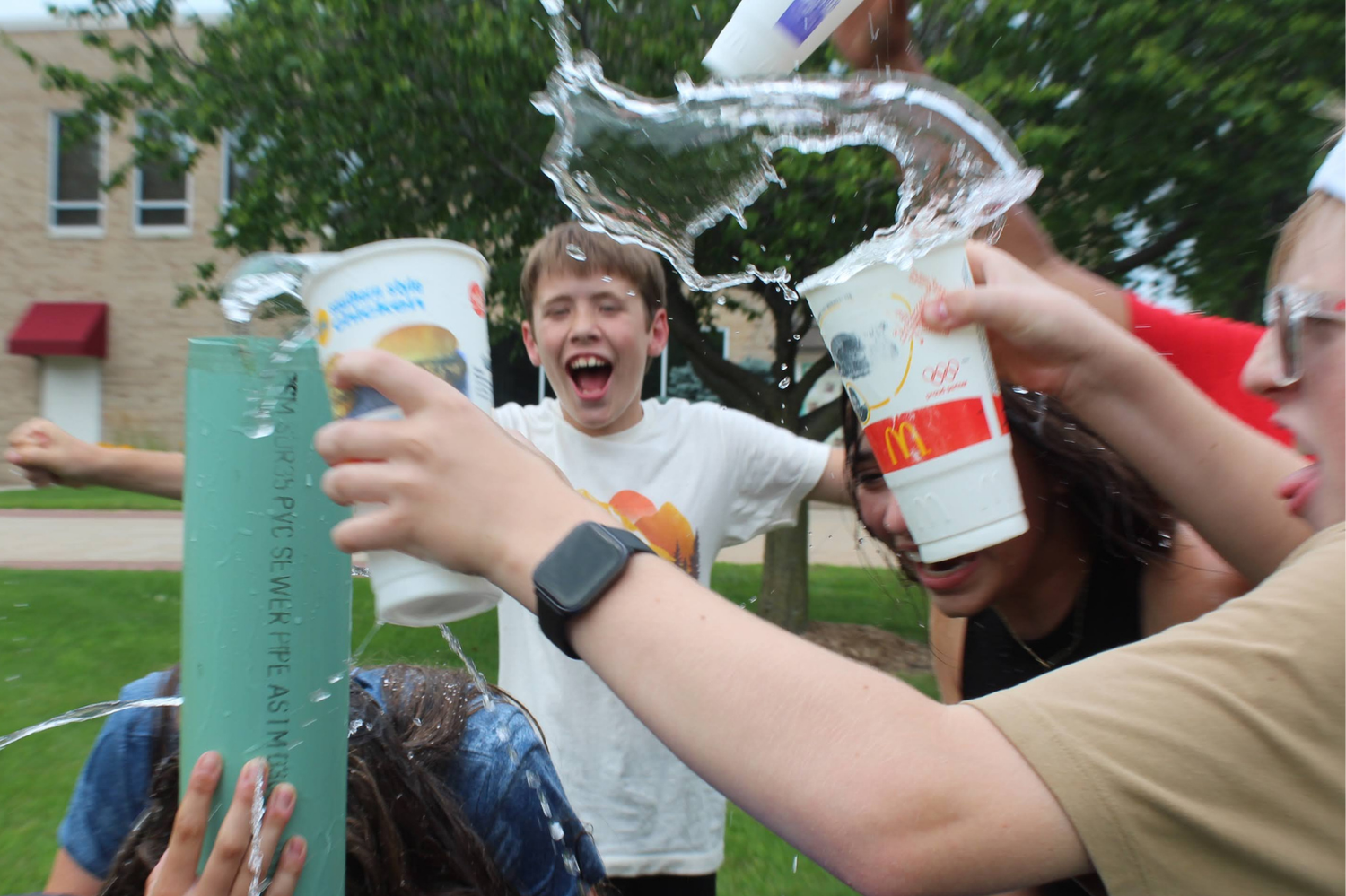 Excited students pour water from cups during a fun outdoor science experiment on a sunny day.