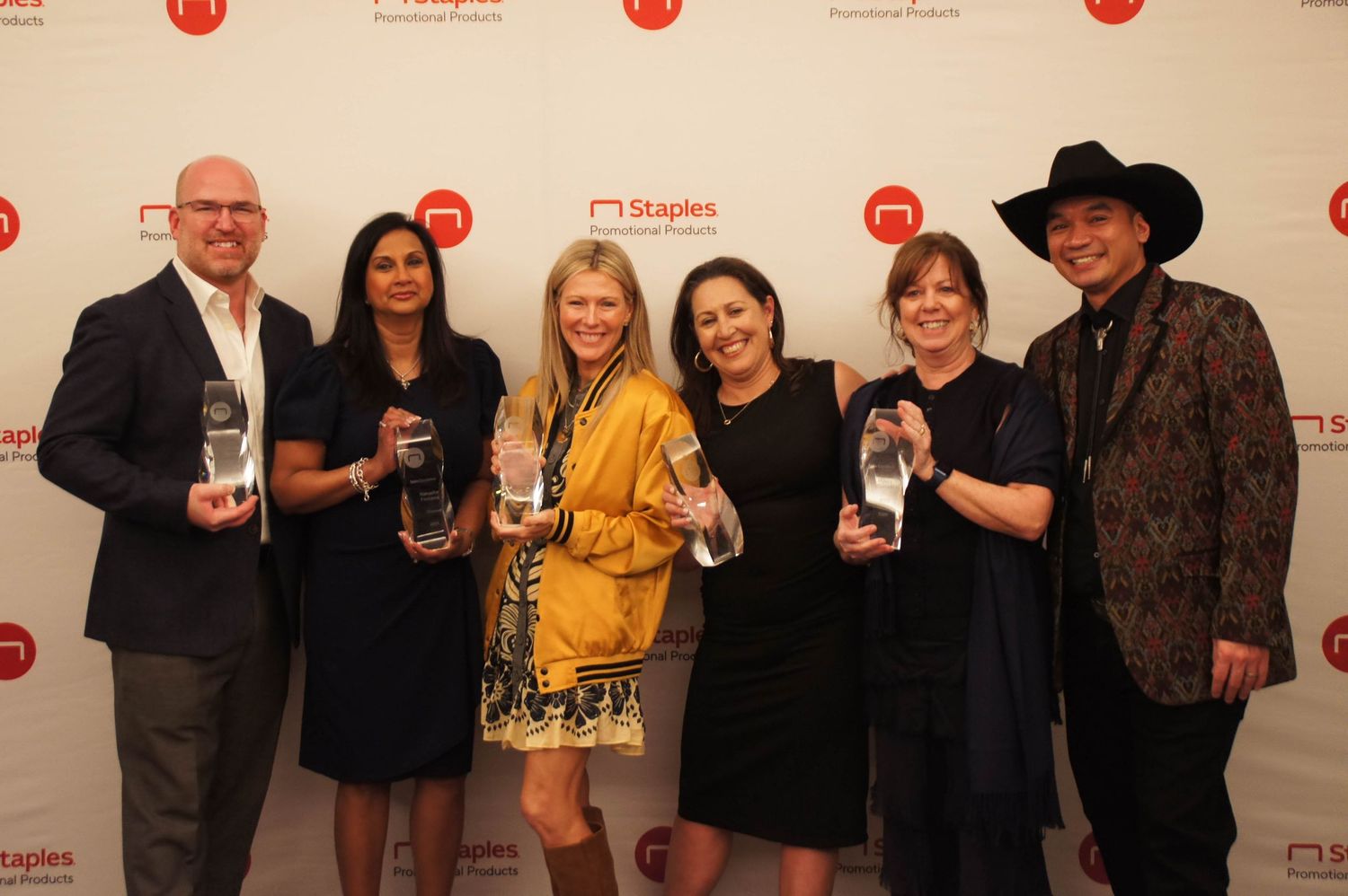Group of six professionals pose together holding crystal awards at Staples promotional event.