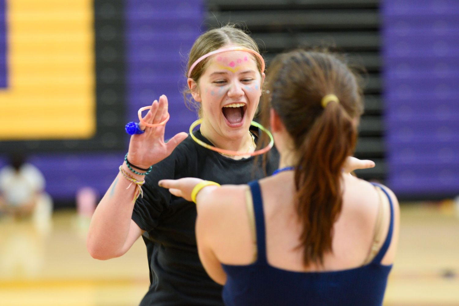 Two excited young women high-fiving in a school gymnasium wearing blue and gold athletic wear.